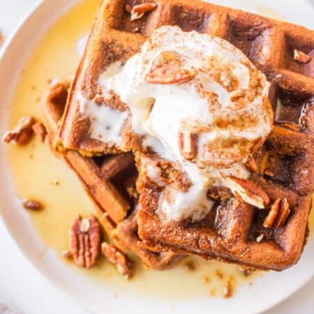 Two stacked gingerbread waffles topped with whipped cream and pecans.