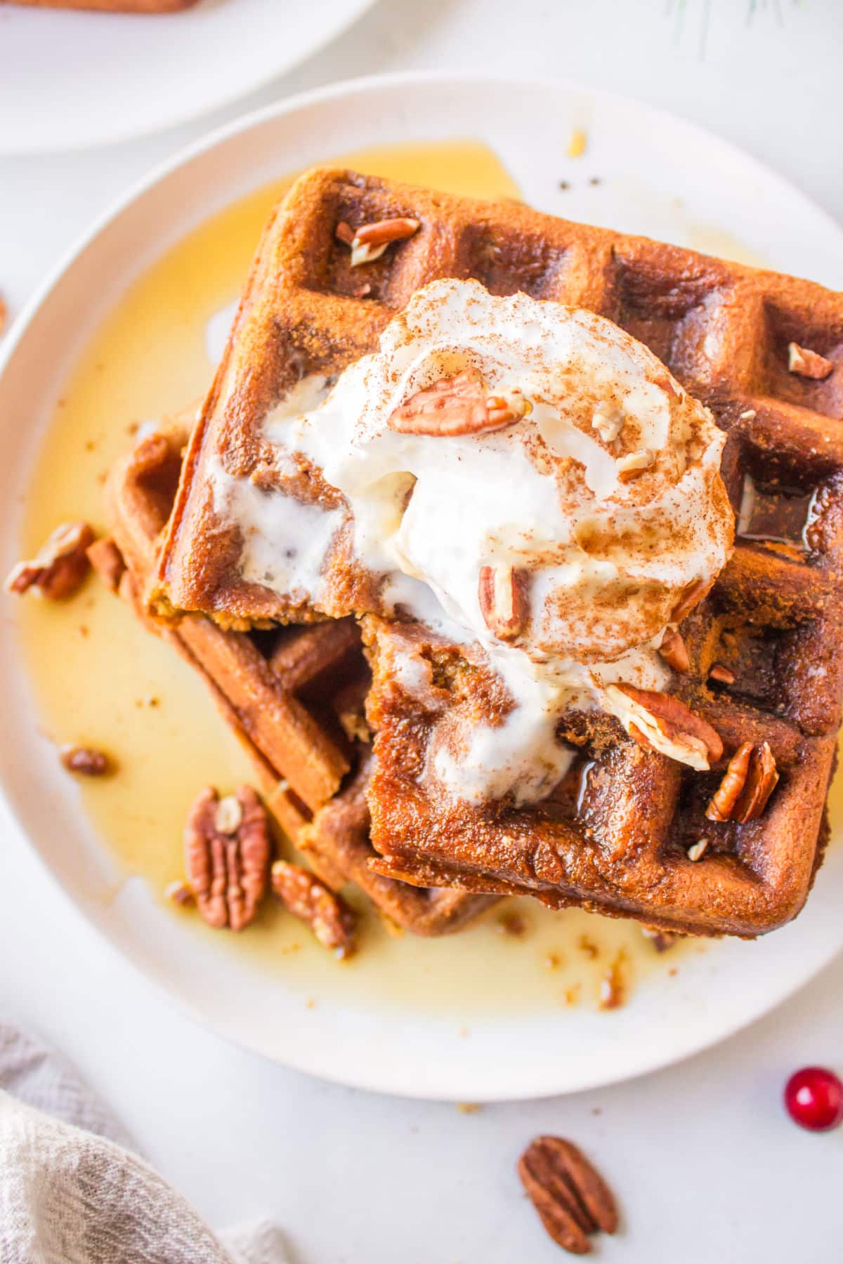 Two stacked gingerbread waffles topped with whipped cream and pecans.