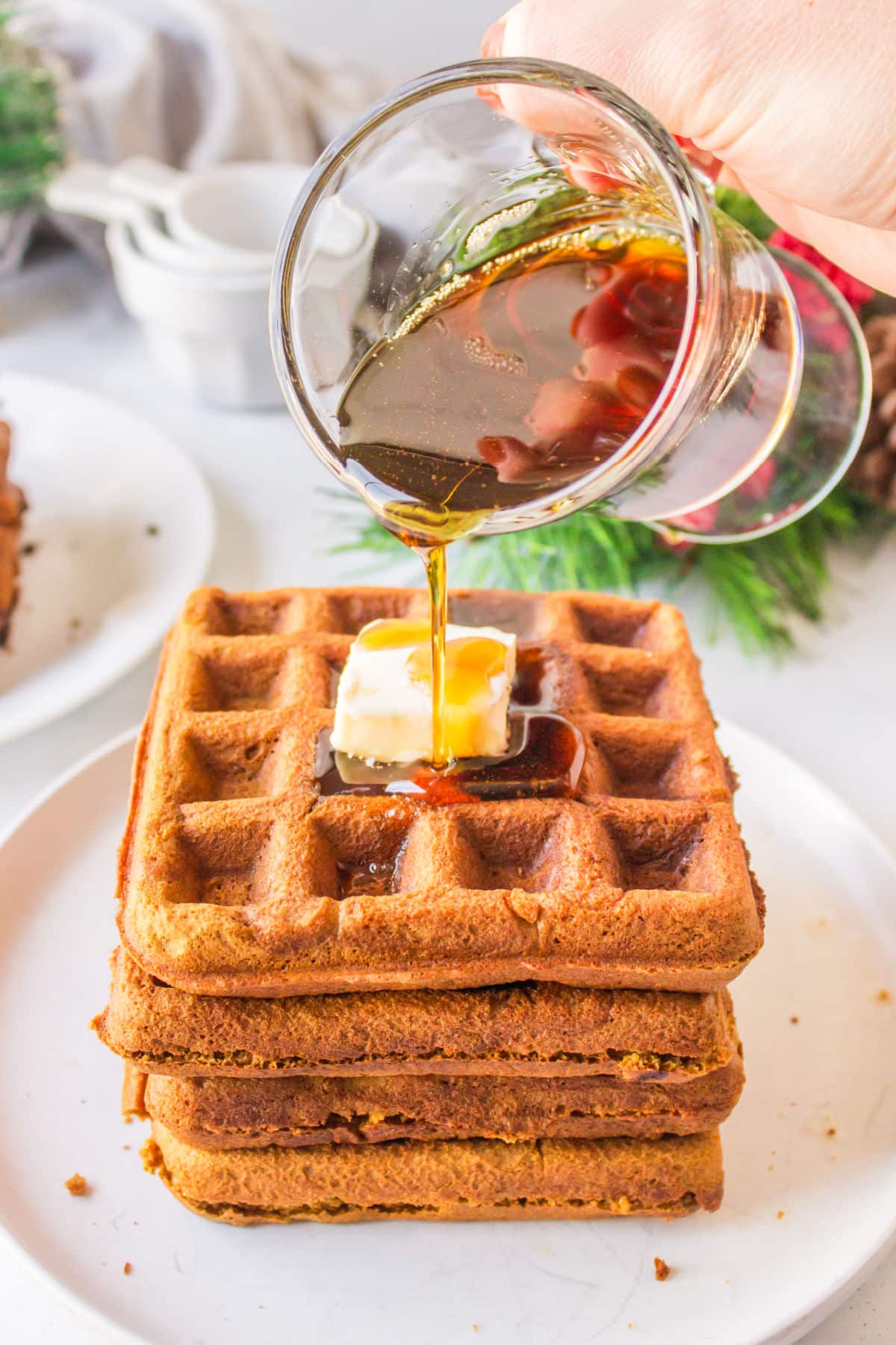 A dish of maple syrup pouring onto a stack of gingerbread waffles.