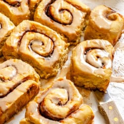 A potato cinnamon roll resting on a knife on parchment paper.