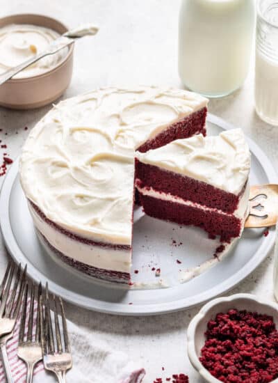 A red velvet layer cake with cream cheese frosting next to a bowl of frosting.