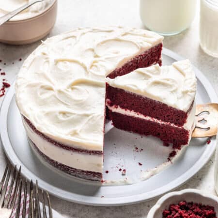A red velvet layer cake with cream cheese frosting next to a bowl of frosting.
