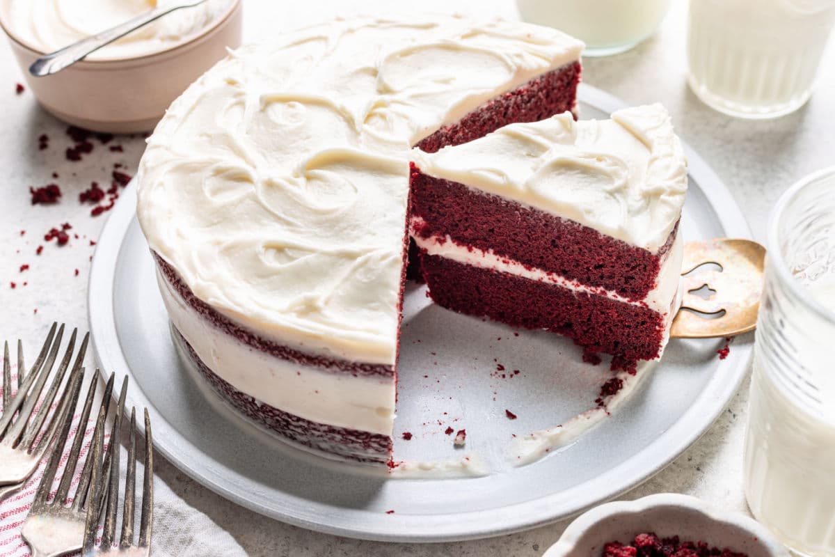 A red velvet layer cake on a platter with pieces cut.