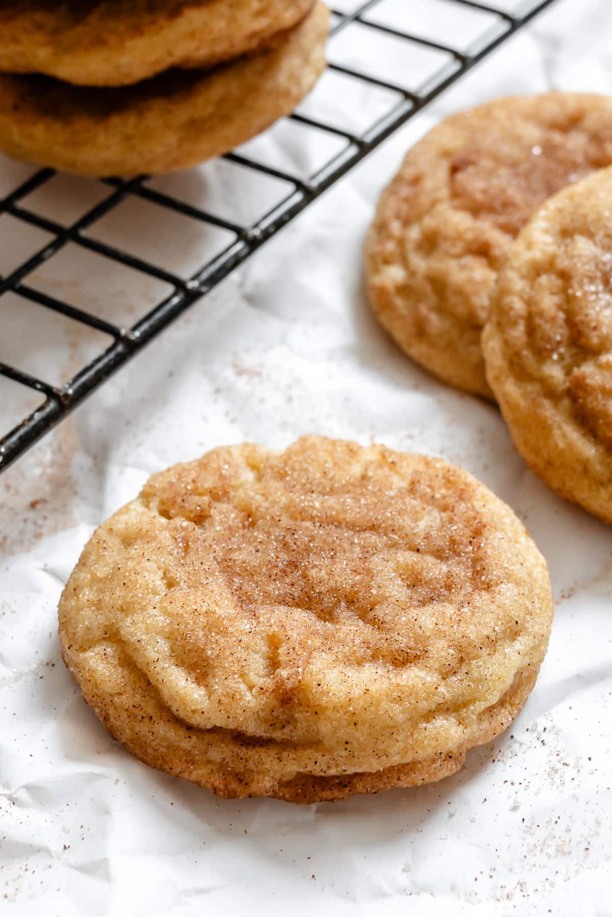 Chewy Snickerdoodles A snickerdoodle cookie next to a cooling rack with cookies on it.