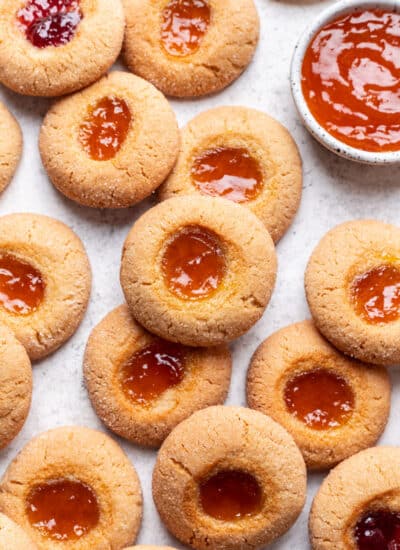 Overlapping rows of thumbprint cookies next to a small dish of jam.