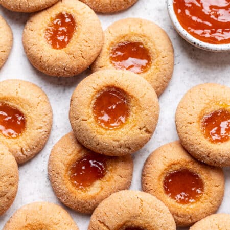 Overlapping rows of thumbprint cookies next to a small dish of jam.