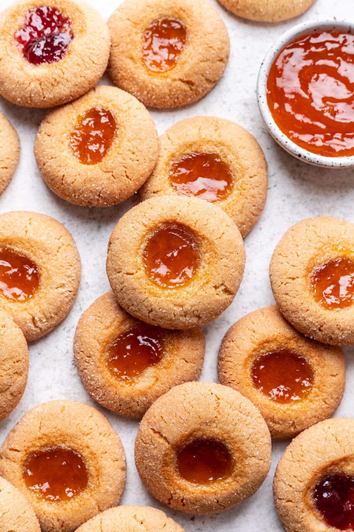 Overlapping rows of thumbprint cookies next to a small dish of jam.