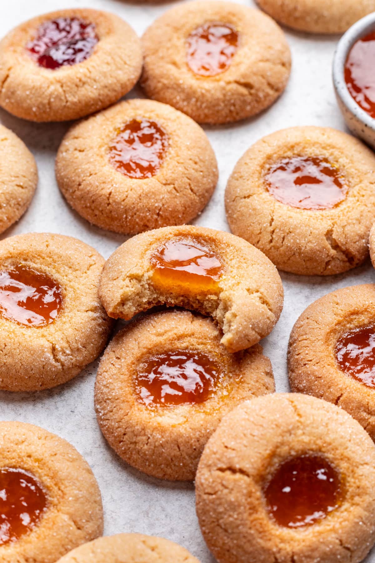 A thumbprint cookie with a bite missing leaning against other thumbprint cookies. 