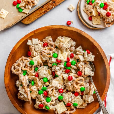 A bowl of Christmas chex mix next to a dish cloth.