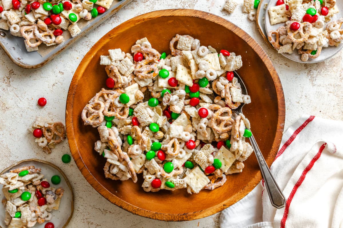 A silver spoon in a wooden bowl of Christmas Chex mix. 