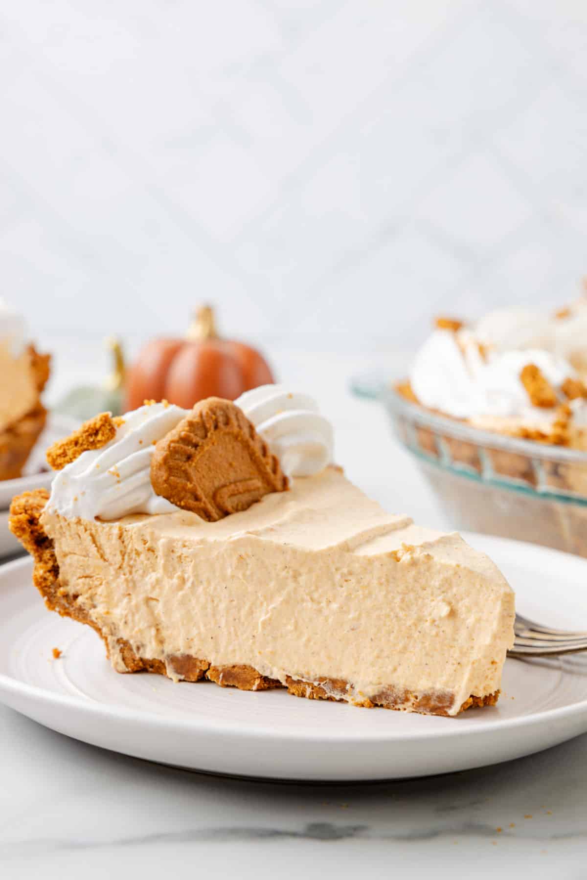 A slice of no bake pumpkin pie topped with whipped cream and a Biscoff cookie.