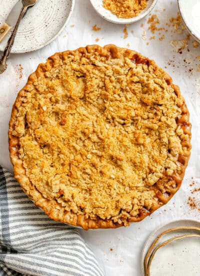 An apple crumble pie next to a stacked plates and silverware.