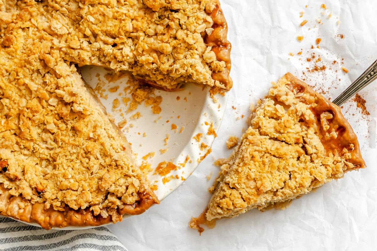 A pie server holding a slice of apple crumble pie next to the pie pan.