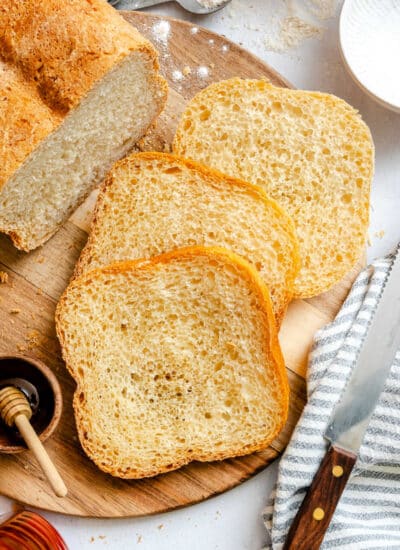 Three slices of honey white bread next to the loaf.