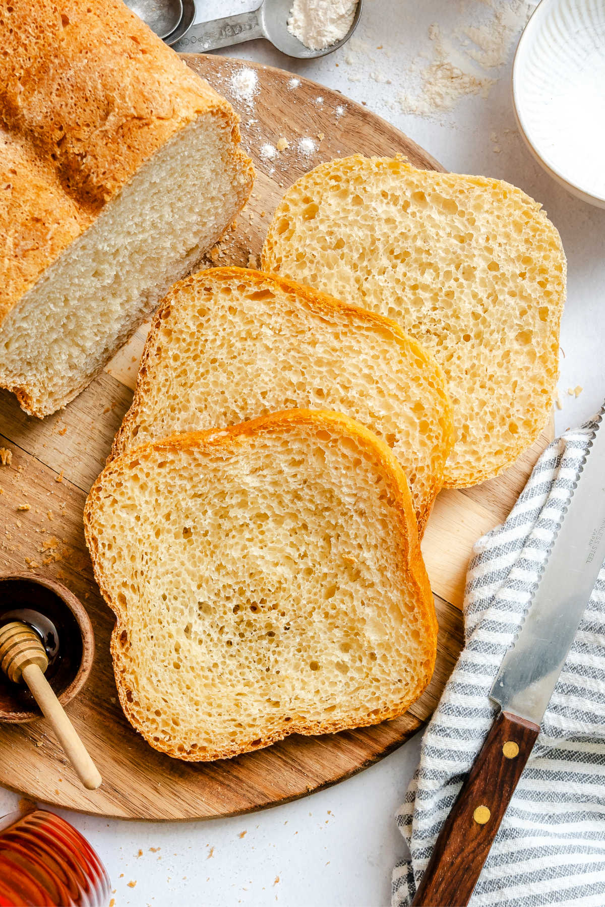 Three slices of honey white bread next to the loaf.