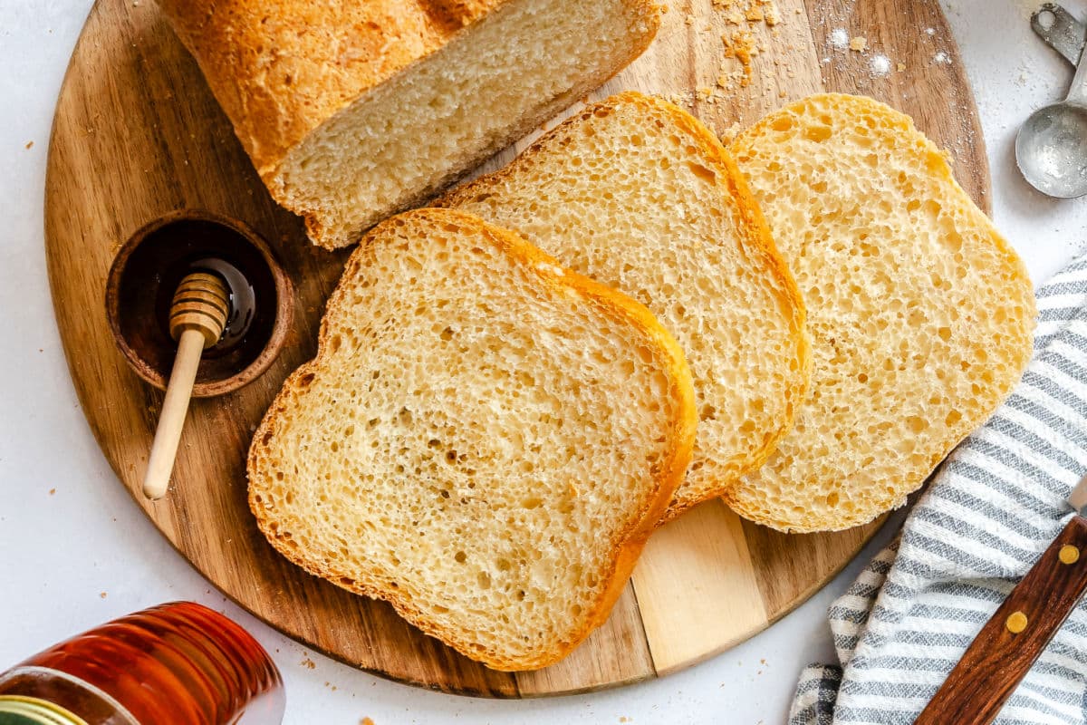Slices of bread machine honey white bread next to honey and a honey dipper.