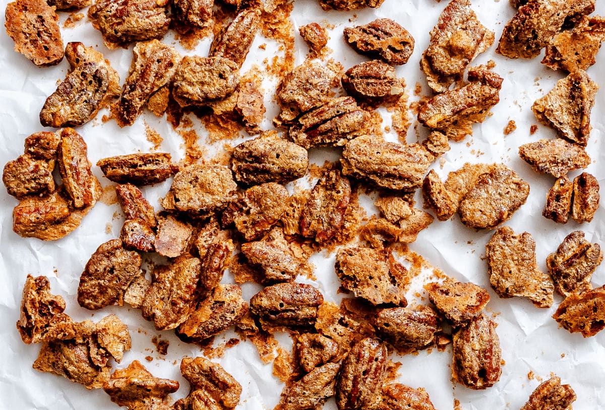 Overlapping candied pecans cooling on a piece of parchment paper.