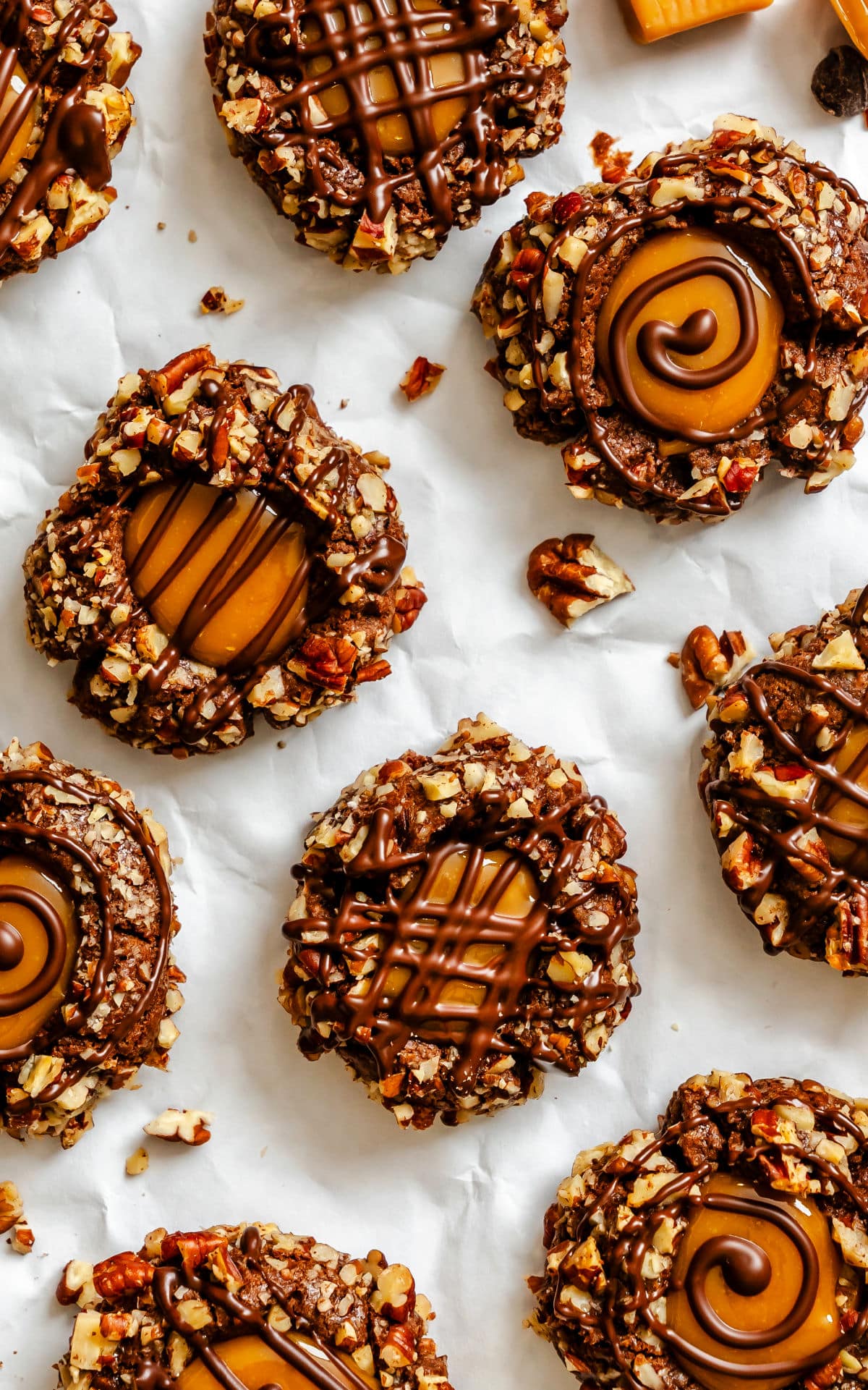 Chocolate caramel thumbprint cookies on a piece of white parchment paper.