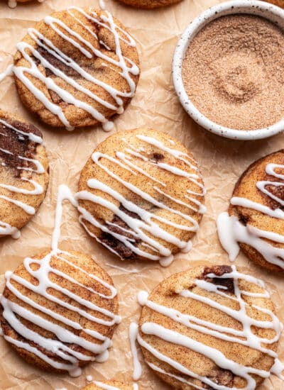 Iced cinnamon roll cookies on a piece of brown parchment paper.