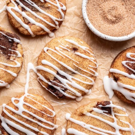 Iced cinnamon roll cookies on a piece of brown parchment paper.