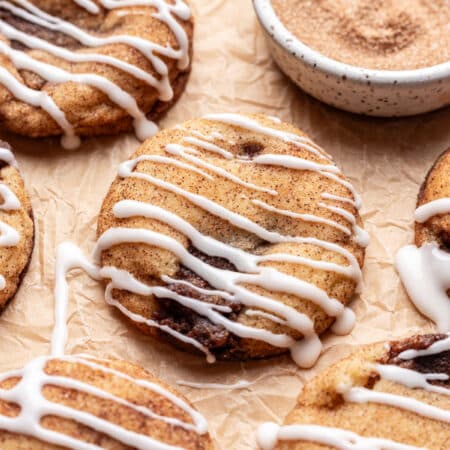 Iced cinnamon roll cookies next to a dish of cinnamon sugar.