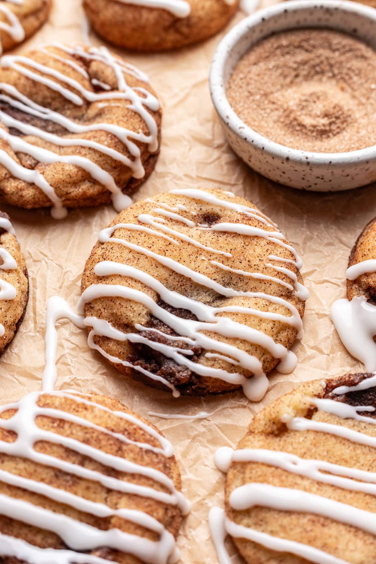 Iced cinnamon roll cookies next to a dish of cinnamon sugar. 