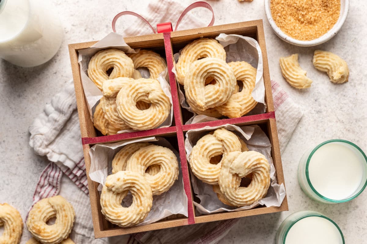 A box of Danish butter cookies next to a glass of milk and a dish of raw sugar.