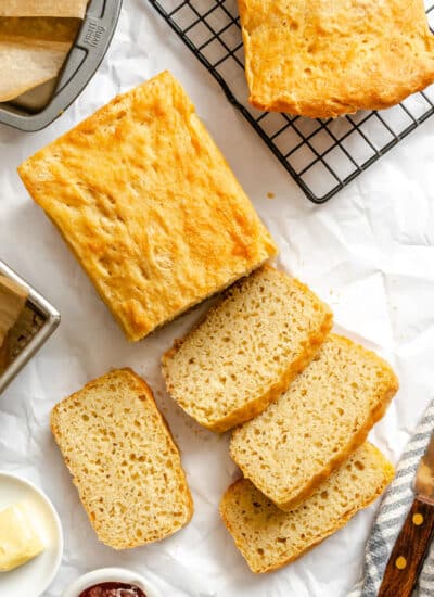 Slices of English muffin bread in a row next to the loaf and another loaf on a wire rack.