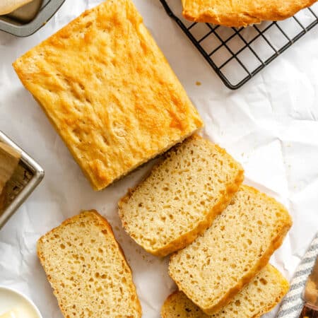 Slices of English muffin bread in a row next to the loaf and another loaf on a wire rack.