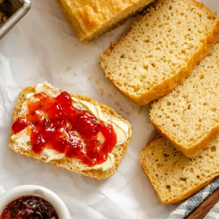 A slice of English muffin bread with butter and jelly next to more slices.