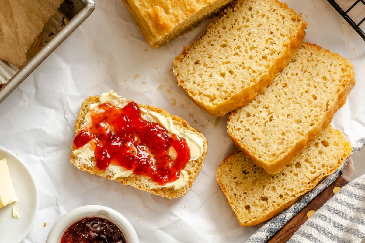 A slice of English muffin bread with butter and jelly next to more slices. 