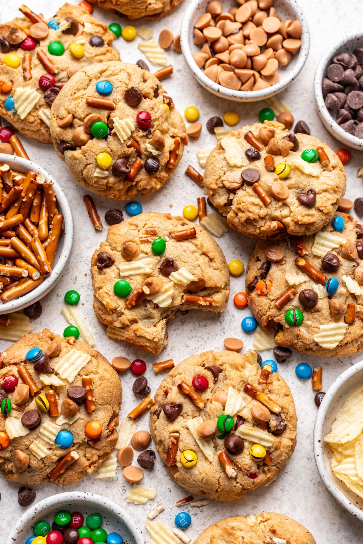Overlapping kitchen sink cookies with dishes of chocolate chips, pretzels, and M&Ms in between.