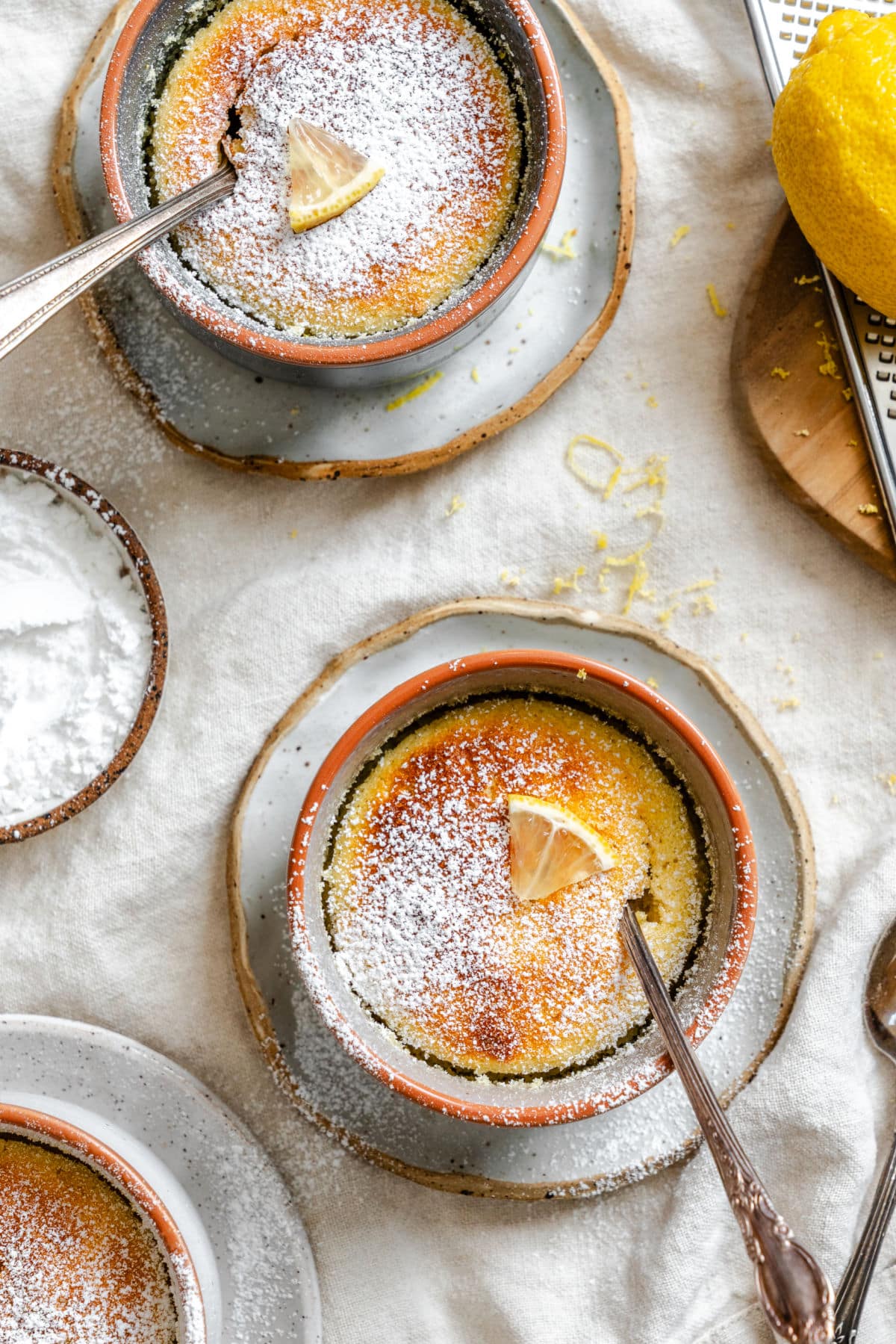 Two lemon pudding cakes dusted with powdered sugar with spoons in them. 