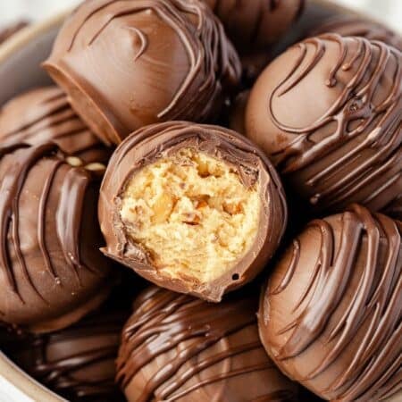 A peanut butter ball with a bite missing in a bowl of peanut butter balls.