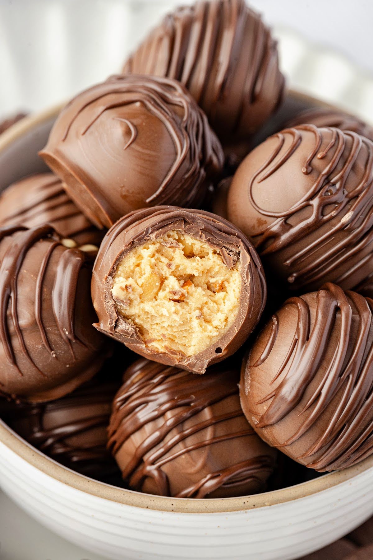 A peanut butter ball with a bite missing in a bowl of peanut butter balls.
