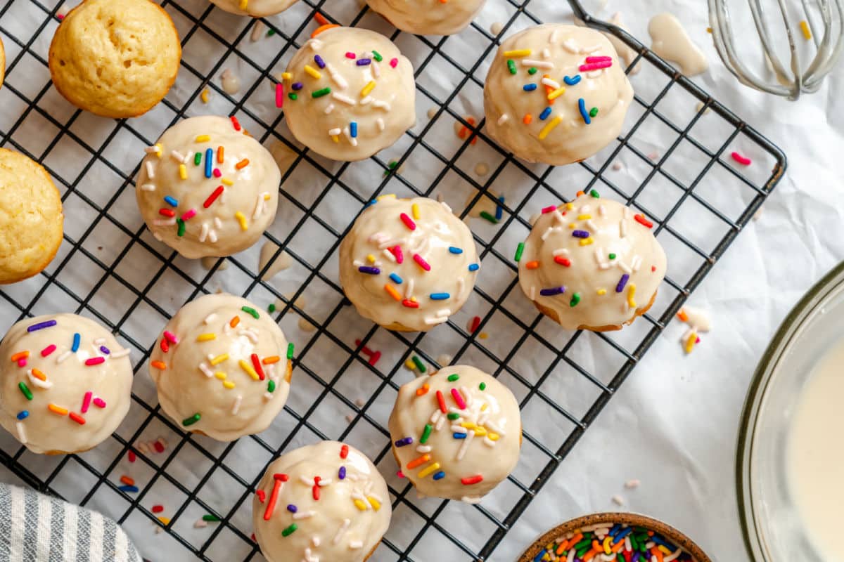 Sugar cookie donut holes next to a dish of frosting and a dish of sprinkles. 