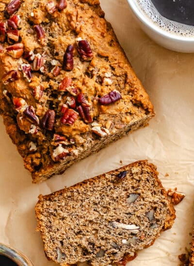 A slice of whole wheat banana bread next to the loaf and a mug of coffee.