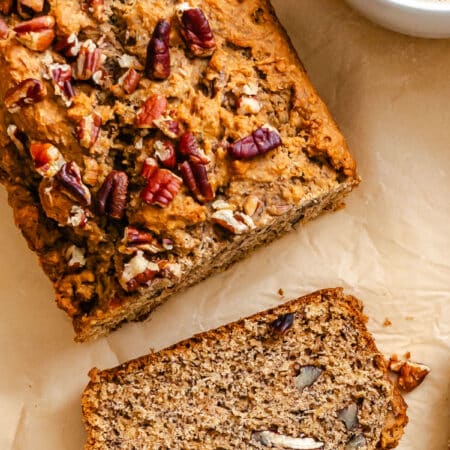 A slice of whole wheat banana bread next to the loaf and a mug of coffee.