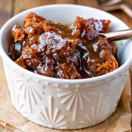 A ramekin with gingerbread pudding cake in it and a gold spoon in the pudding.