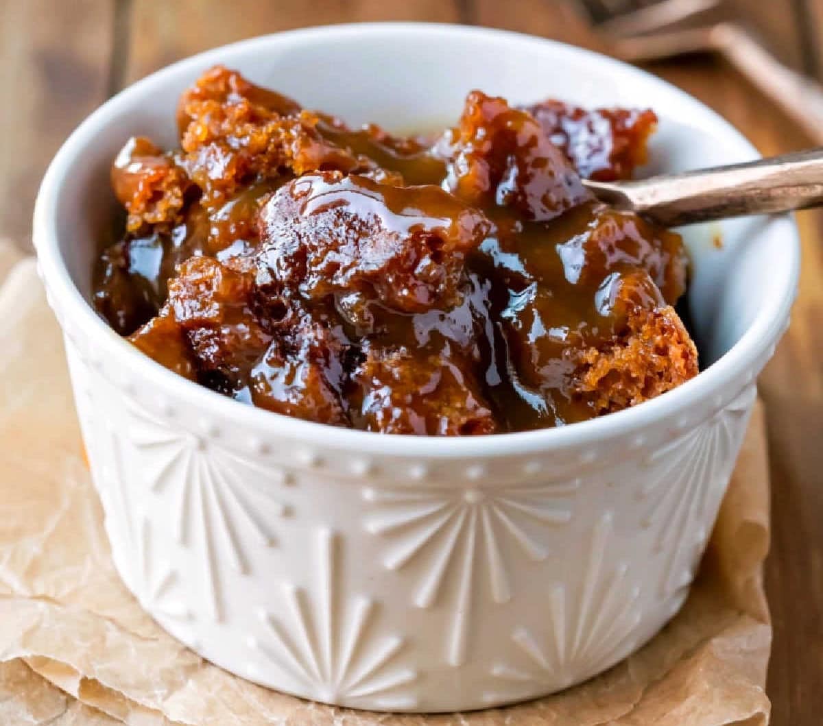 A ramekin with gingerbread pudding cake in it and a gold spoon in the pudding.