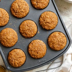 Applesauce muffins in a muffin tin next to a white bowl with a whisk in it.