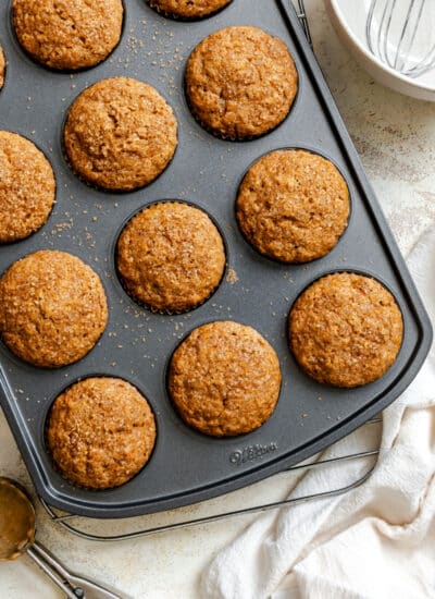 Applesauce muffins in a muffin tin next to a white bowl with a whisk in it.