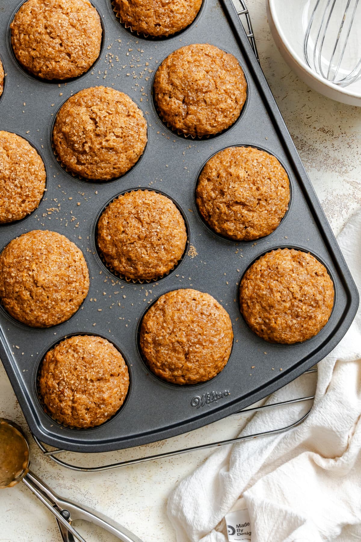 Applesauce muffins in a muffin tin next to a white bowl with a whisk in it.