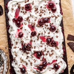 A Black Forest sheet cake on a piece of tan parchment paper next to a bowl of cherries.