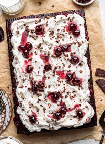 A Black Forest sheet cake on a piece of tan parchment paper next to a bowl of cherries.