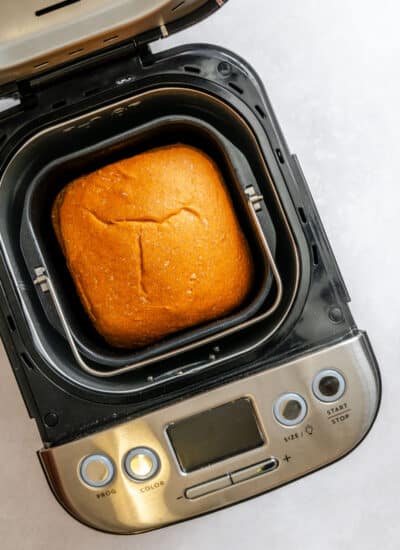 A baked loaf of honey wheat bread in a pan in a bread machine.