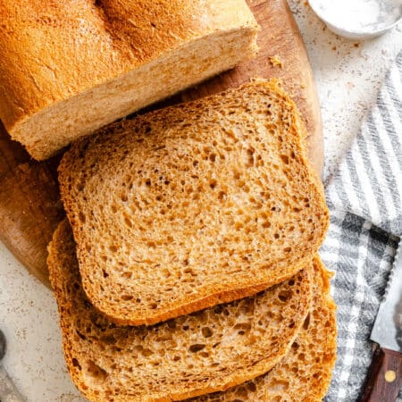 Three slices of steakhouse brown bread sliced next to the loaf.