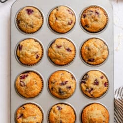 A muffin tin with baked cherry muffins next to a bowl of cherries.
