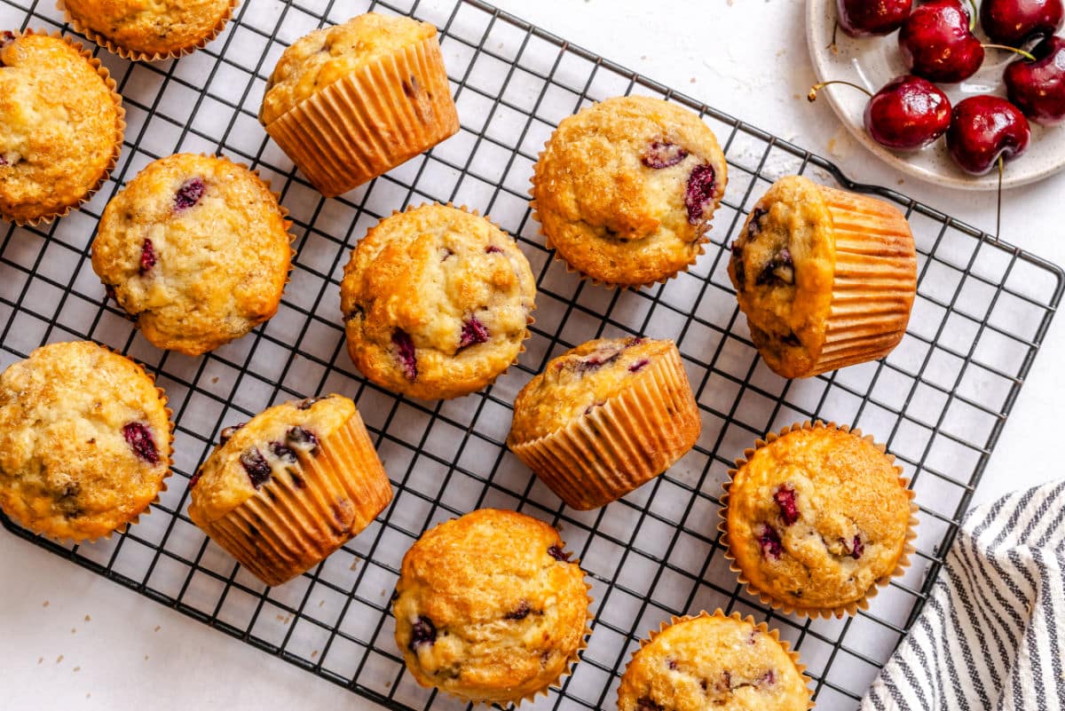 Cherry muffins on a wire rack next to a bowl of fresh cherries.