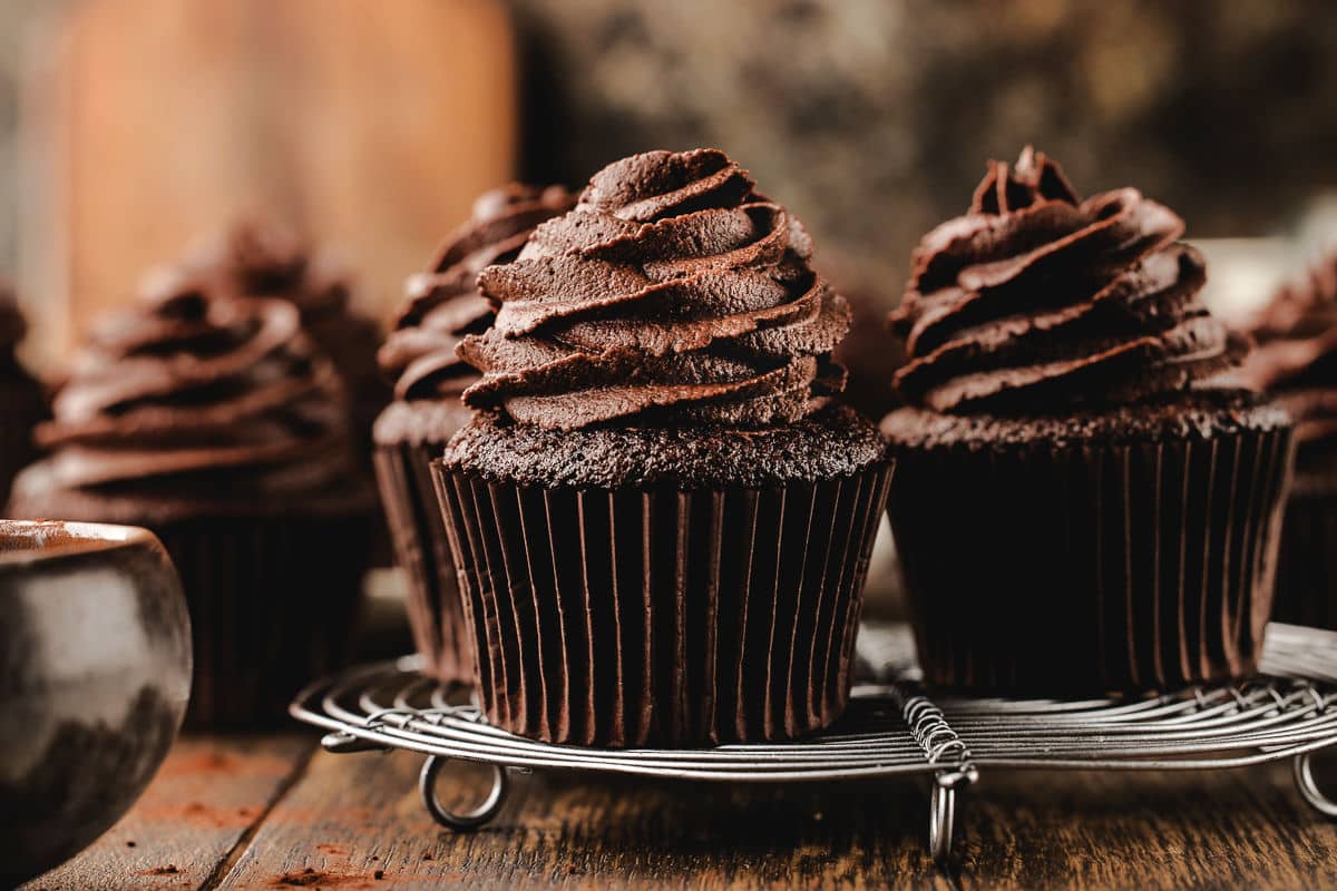 Chocolate cupcakes with piped chocolate buttercream frosting on a wire cooling rack. 